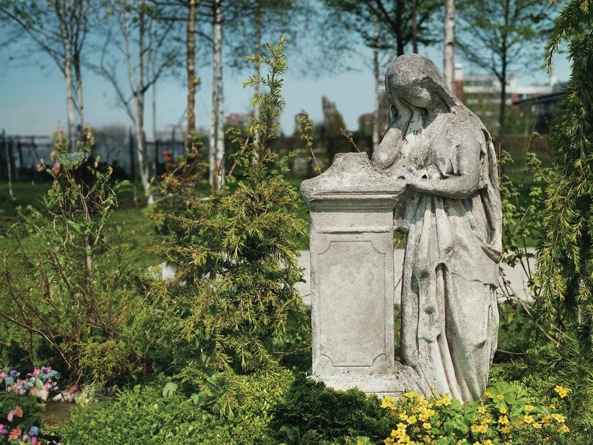 Ein alter aus einem Stein gefertigeter Grabstein an dem eine stilisierte Frau, bzw. ein Engel lehnt und trauert